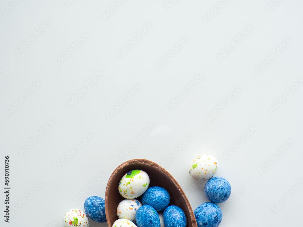 Sweet Easter concept. Blue, white and chocolate easter eggs with sweet dragee on white background with copy space. Design for a greeting card for the Easter holiday. Flat lay. Preparation for holiday.
