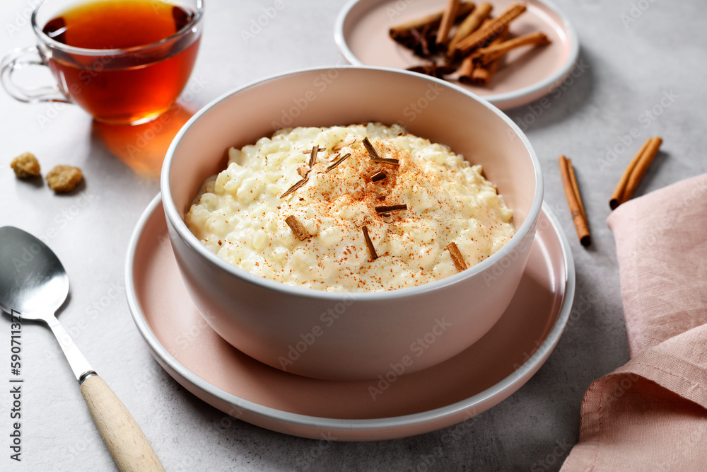 Fresh prepared rice pudding garnished with cinnamon flakes and served with cup of tea. Healthy breakfast for every day. Gray background. Fresh prepared rice pudding garnished with cinnamon flakes and served with cup of tea. Healthy breakfast for every day. Gray background.