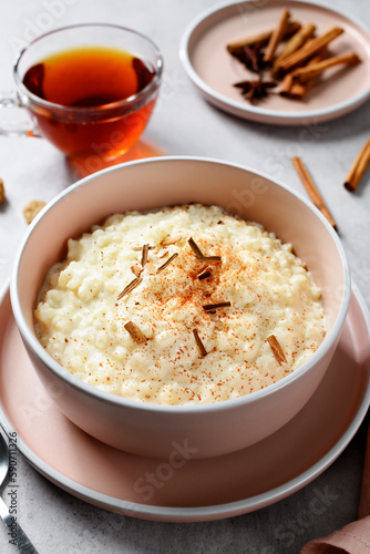 Fresh prepared rice pudding garnished with cinnamon flakes and served with cup of tea. Healthy breakfast for every day. Gray background.