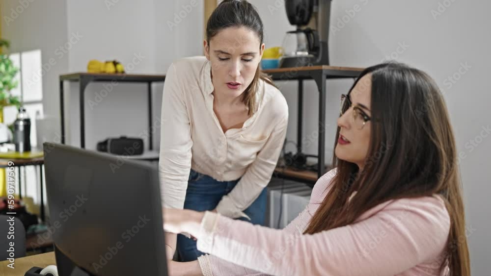 Two women business workers using computer speaking at office Two women business workers using computer speaking at office