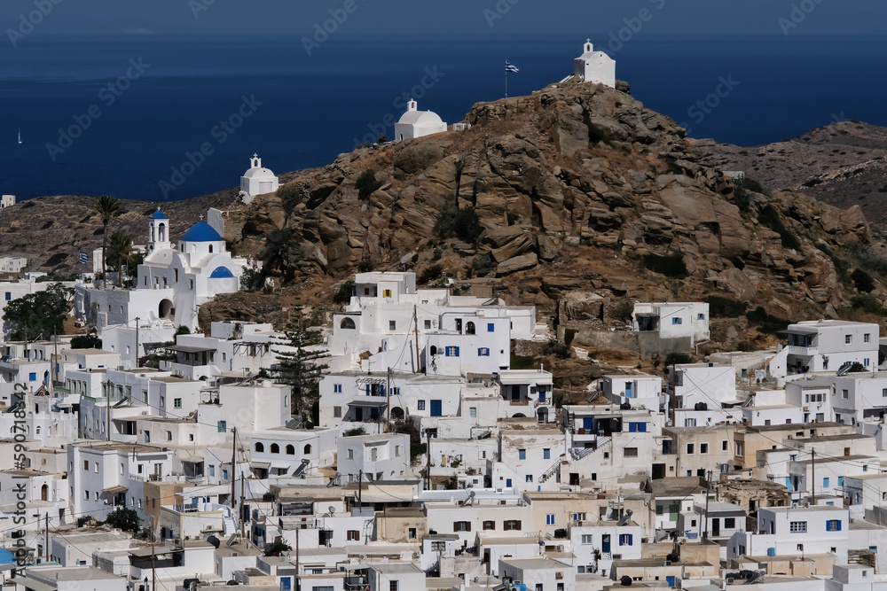 Panoramic view of a church, smaller chapels and the Greek flag on the top of a hill overlooking the Aegean Sea in  Ios in Greece, also known as Chora