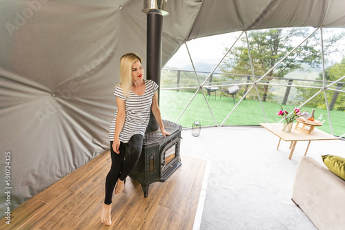 a woman is soldering near the fireplace in the transparent dome of the glamping hotel