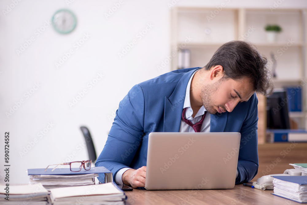 Young male employee unhappy with excessive work in the office Young male employee unhappy with excessive work in the office