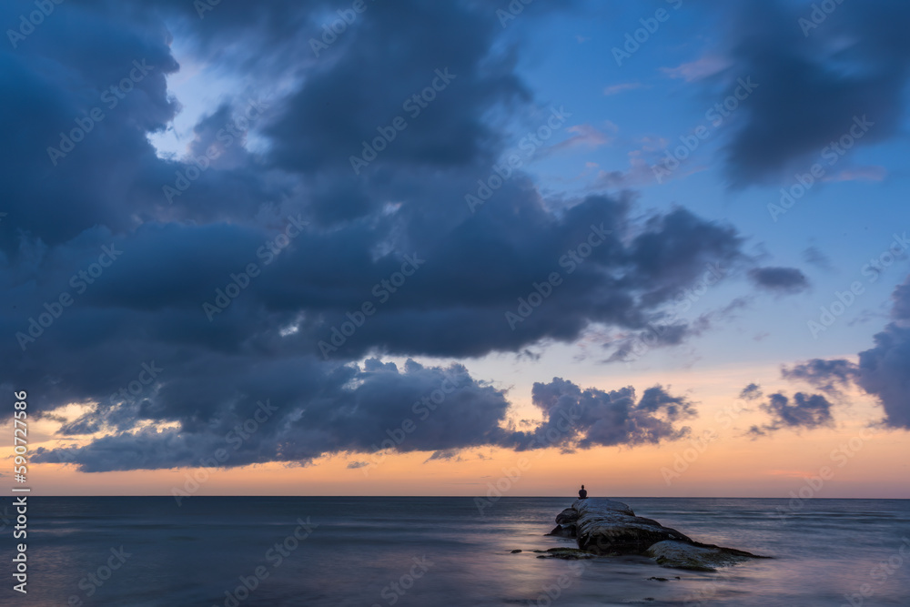Atemberaubender Strand-Sonnenuntergang mit dramatischem Himmel und einem Mann auf einem Felsensteg Atemberaubender Strand-Sonnenuntergang mit dramatischem Himmel und einem Mann auf einem Felsensteg