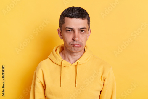 Sad disappoiinted upset man wearing casual hoodie being bad mood offended looking at camera with pout lips posing isolated over yellow background.