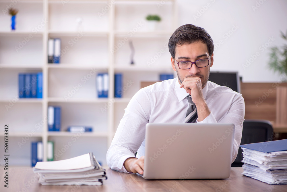 Young male employee unhappy with excessive work at workplace Young male employee unhappy with excessive work at workplace