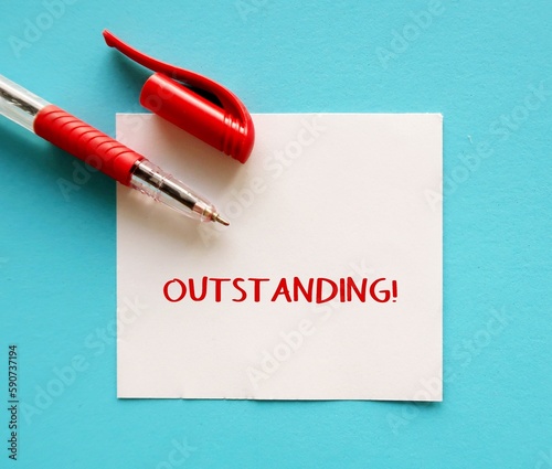 Red pen writing on note on blue background with handwritten OUTSTANDING!, compliment praise giving to someone to tell they are doing great work or awesome job, Boss admire worker for impressive job