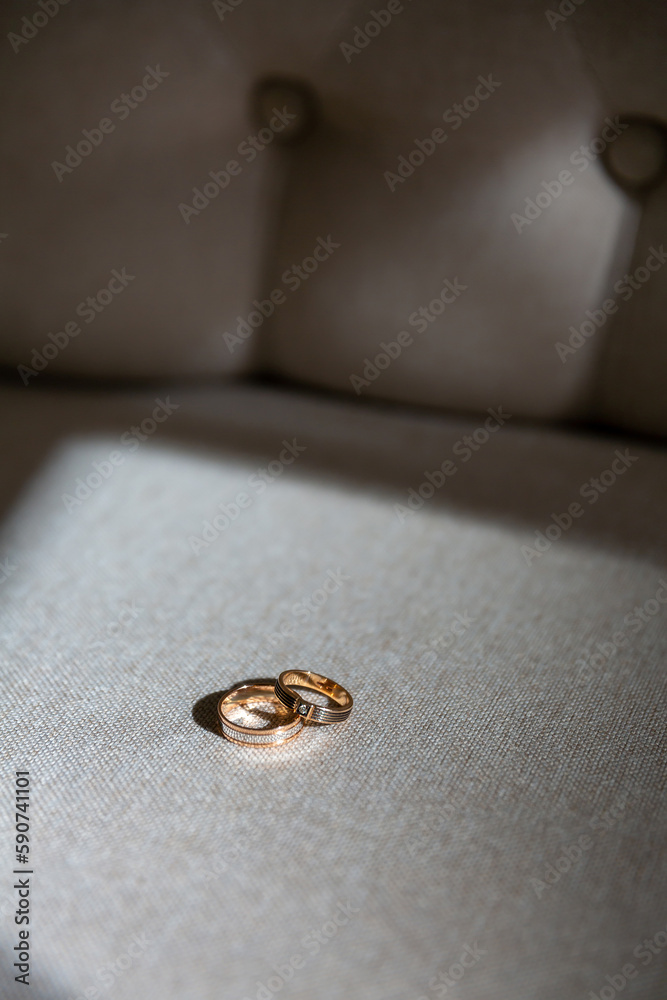 wedding rings lie on the sofa, illuminated by bright contrasting rays of the sun. The concept of family life and happiness wedding rings lie on the sofa, illuminated by bright contrasting rays of the sun. The concept of family life and happiness