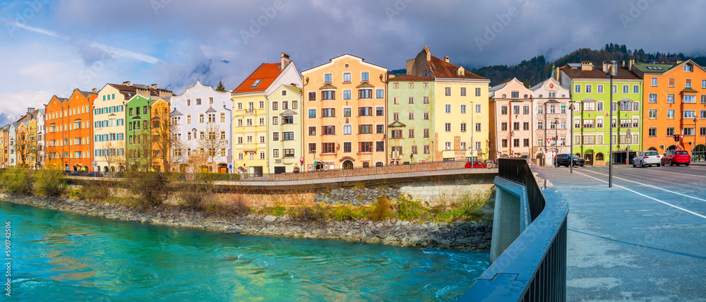 Innsbruck city skyline on a April day with vibrant colorful houses, the snowy Alps mountains, foggy cloudscape, the green Inn River in historic landmark town of Tyrol in western Austria
