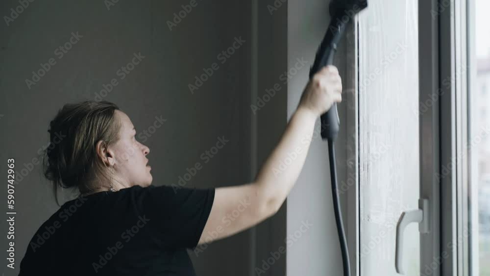 A woman washes a window with a steam cleaner. Room cleaning. A woman washes a window with a steam cleaner. Room cleaning.