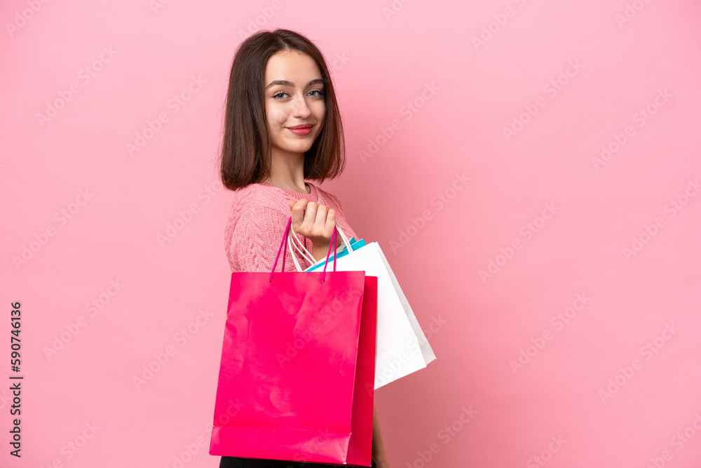 Young Ukrainian woman isolated on pink background holding shopping bags and smiling