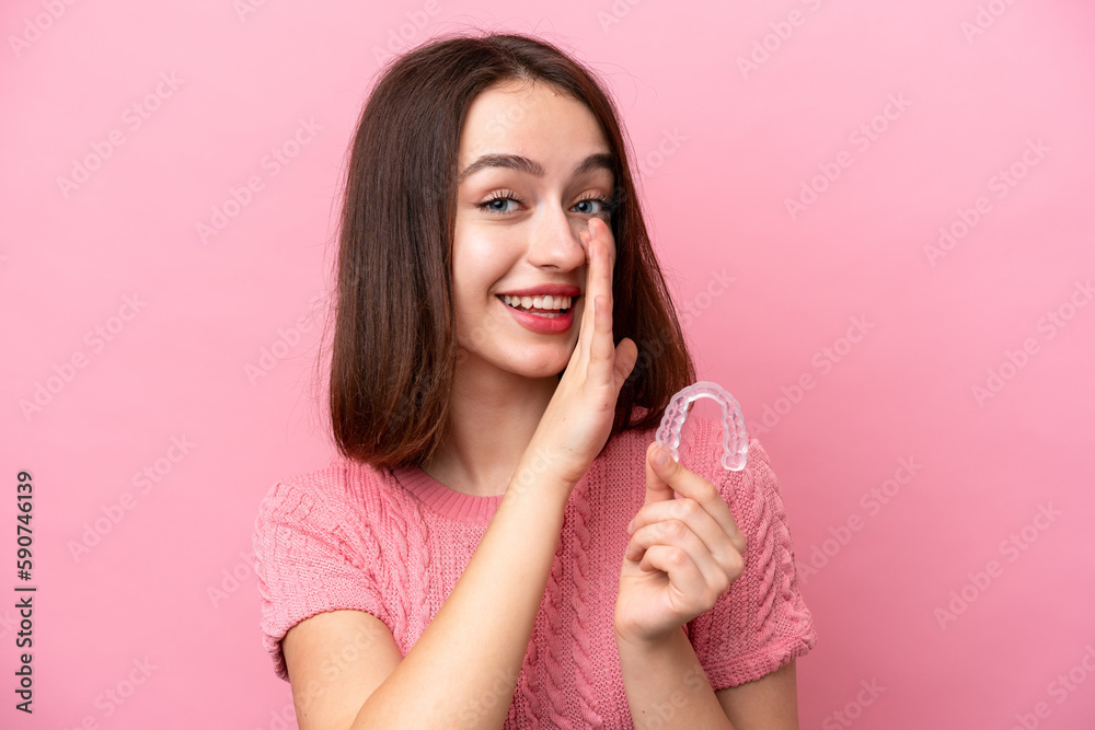 Young Ukrainian woman holding invisible braces isolated on pink background whispering something Young Ukrainian woman holding invisible braces isolated on pink background whispering something