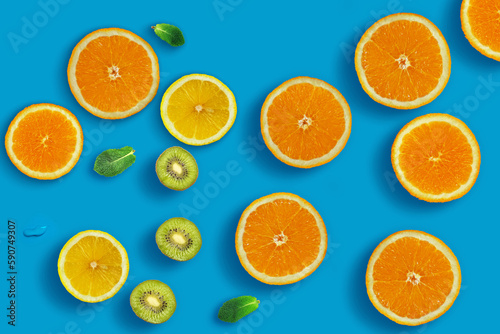 Fresh juicy slices of orange  kiwi fruit  lemon and mint leaves on bright blue background. Creative food background  top view