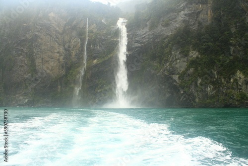 Teal color sea with a waterfall in the background. Milford Sound, New Zealand.