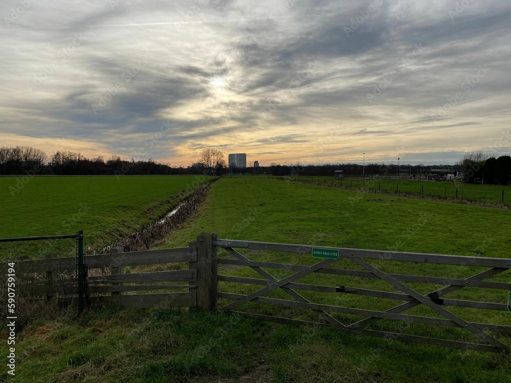 Fields with wooden fence and dramatic sunset cloudy sky on the horizon