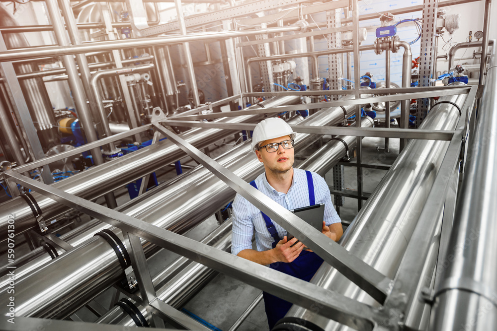 Top view of engineered metal structures of pipelines. Industrial plant for the treatment contaminated wastewater. A young engineer inspects the system using a tablet pc. Top view of engineered metal structures of pipelines. Industrial plant for the treatment contaminated wastewater. A young engineer inspects the system using a tablet pc.