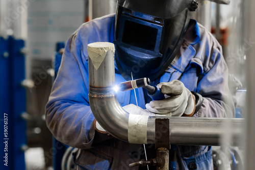 Male in face mask welds with argon-arc welding pipes.