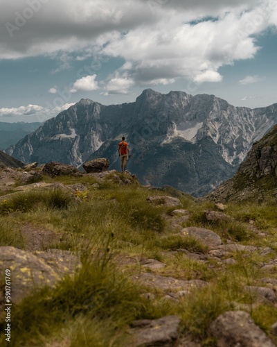 Fototapeta Naklejka Na Ścianę i Meble -  Vertical shot of a person hiking in green mountains under a cloudy blue sky