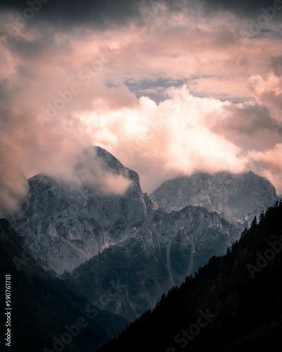 Vertical aerial view of a rocky peak of a green mountain range covered with clouds at sunset