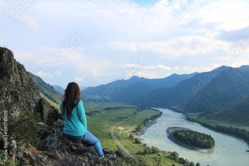 Woman sitting on a hill, looking at Island on the river Katun at summer day. Trip on Altai Republic, enjoyment of nature