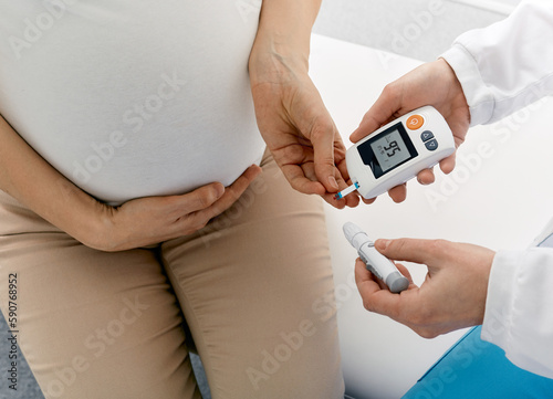 Endocrinologist checking blood sugar level of pregnant woman with gestational diabetes using glucometer in medical clinic during consultation. High blood sugar in pregnant woman photo