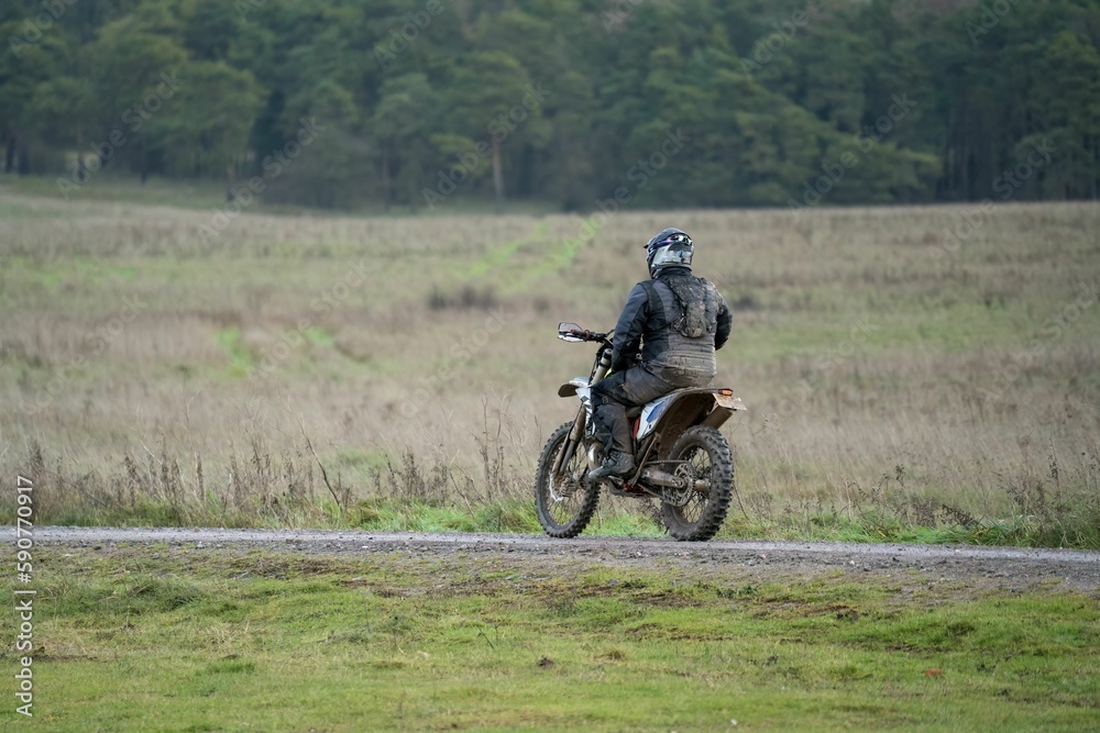 Rear view of a motor cyclist (biker) riding their off-road motorbike along a stone track