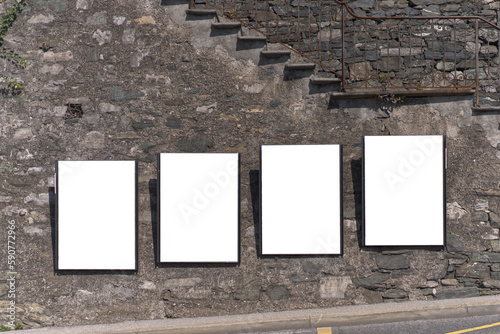 Four empty vertical posters attached to a concrete wall on a steep street. photo