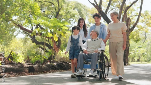 Happy Asian senior man sitting on wheelchair in the park with big family on weekends holiday