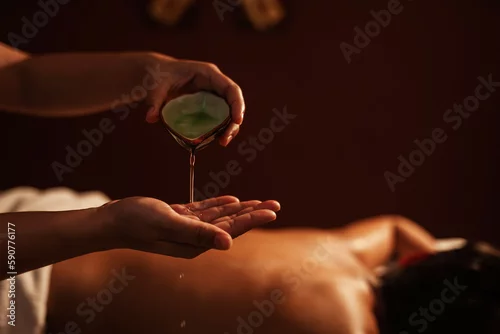 Obraz Masseur pouring aroma oil on hand, for massage on back of customer. Relaxation young male customer get service aromatherapy massage with masseuse in spa salon.