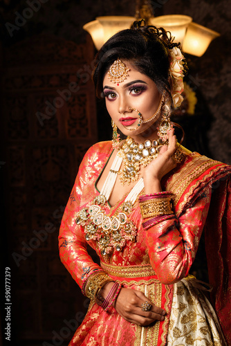 Magnificent young Indian bride in luxurious bridal costume with makeup and heavy jewellery with classic vintage interior in studio lighting. Wedding Fashion and Lifestyle.