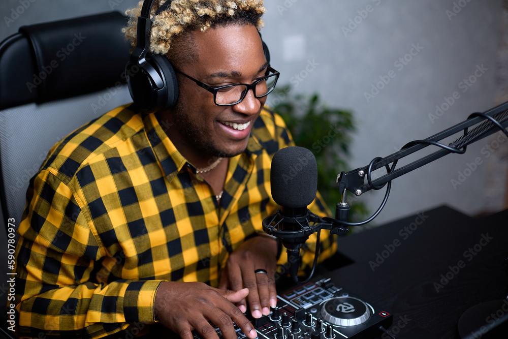 An African-American man works in a radio studio. Black-skinned male radio  host transmits the news and speak into the microphone. A DJ with an African  hairstyle puts on music for listeners. Stock