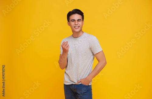 Happy smiling asian man celebrating victory, chanting yes with hands raised up and broad grin, triumphing over achievement or success isolated on yellow studio background.