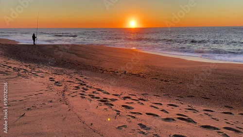 Unidentifiable man in silhouette, fishing on the beach at sunset. Beautiful sunset in late spring. Fishing rod upright in the sand.