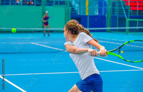 A girl plays tennis on a court with a hard blue surface on a summer sunny day 