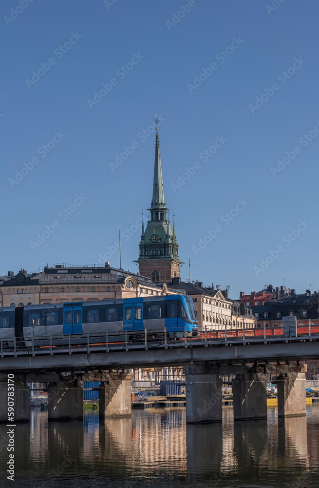 Fototapeta premium Subway on a bridge passing the old town Gamla Stan and the church Tyska kyrkan, a sunny spring morning in Stockholm
