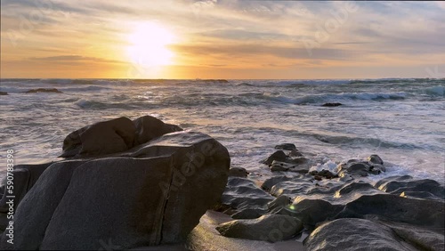 Gentle ocean waves washing over big rocks on the beach in Portugal at sunset. Large boulder in foreground. Beautiful pastel sky.