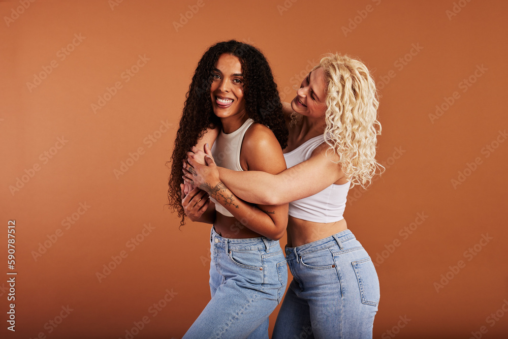 © Flamingo Images - Laughing woman hugging her smiling friend on an orange background © Flamingo Images - Laughing woman hugging her smiling friend on an orange background