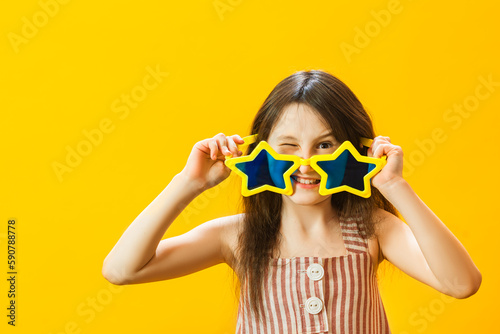 Portrait of little girl isolated on yellow background with funny facial expression. The child wears huge star-shaped glasses. photo