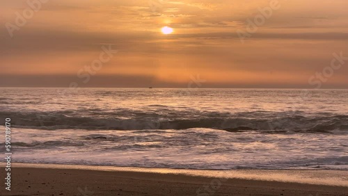 Beautiful calm, sunset over the ocean, with muted, pastel orange shades and small fishing boat bobbing on waves in distance.