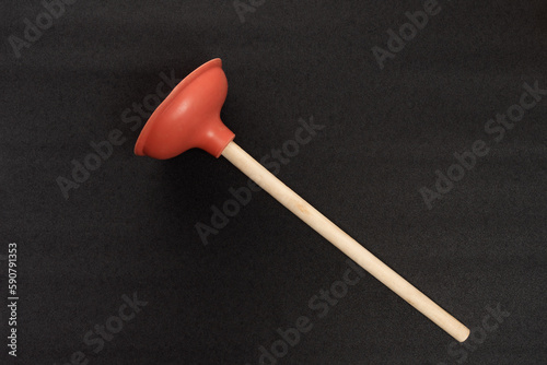 Red toilet plunger with wooden handle isolated on black background. Professional plumber tool.