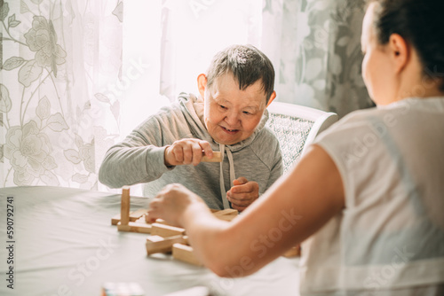 Fototapeta elderly woman with down syndrome and an Asian woman play in tower from wooden bl