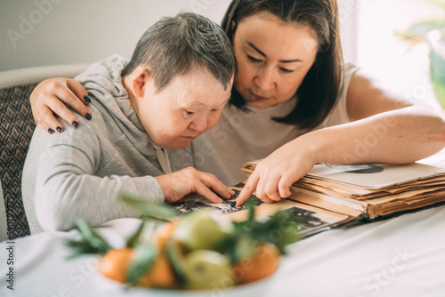 smiling elderly woman with Down syndrome looks at photos in an old album. Save memory