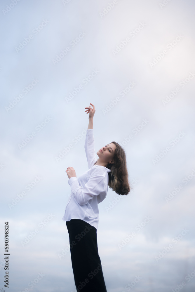Brunette girl with raised arms against the sky