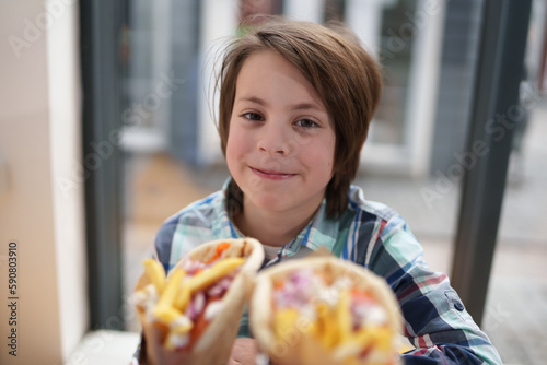 Happy little boy in a fast food restaurant. Portrait of cheerful white kid ready to eat lunch in a Greek diner