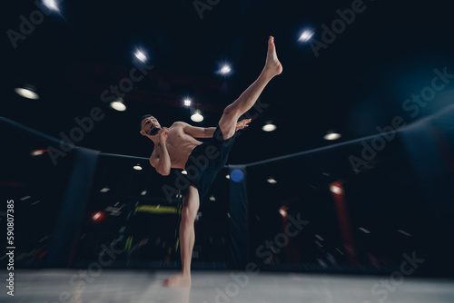 MMA Training of fighter without rules in octagon cage, man makes kick in flight on dark background © Parilov