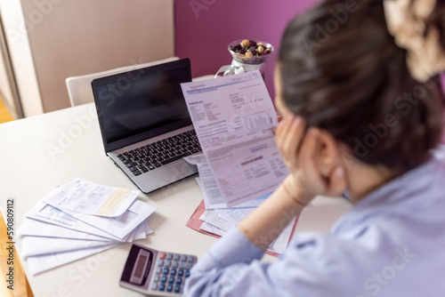 Warried  woman looking at  bills and calculating her monthly expenses and debts. Bankrupt Female having problem income, budget, payment. Paying bills online on laptop at home. Economic crisis photo