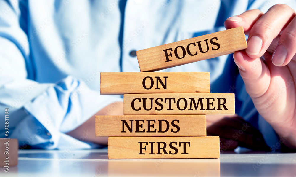 Close up on businessman holding a wooden block with "Focus on customer needs first" message - obrazy, fototapety, plakaty 