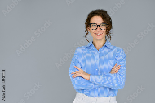 Happy young smiling confident professional business woman wearing blue shirt and glasses, happy pretty female executive looking at camera, standing arms crossed isolated at gray background, portrait.