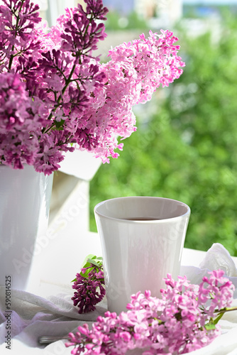 Fototapeta Naklejka Na Ścianę i Meble -  The postcard is beautiful. A mug of tea, an old book and a bouquet of purple lilac. A beautiful still life. Spring time. The concept of Good morning.