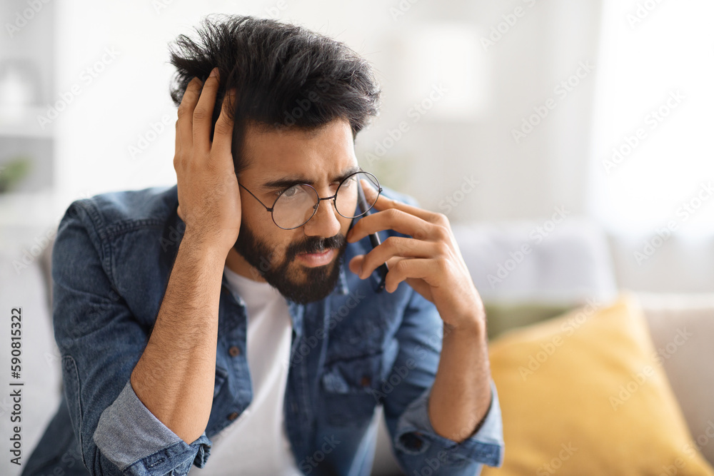 Worried Young Indian Man Talking On Cellphone At Home Worried Young Indian Man Talking On Cellphone At Home